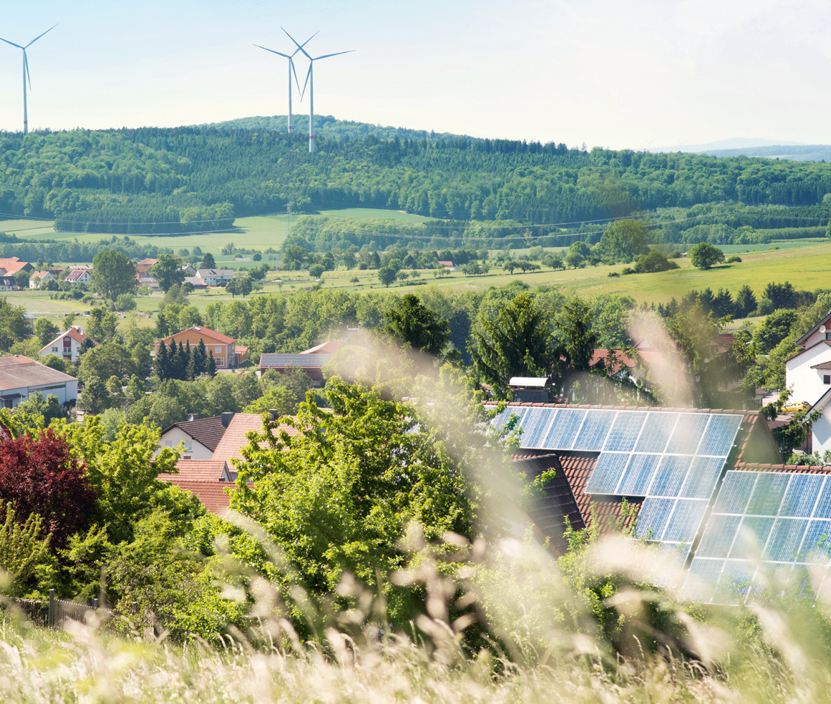 Landschaft mit Häusern mit PV-Anlage und Windrädern im Hintergrund